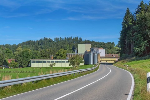 Blue sky, country road, mixed forest and factory with silo towers near Eglofs, Allgäu,