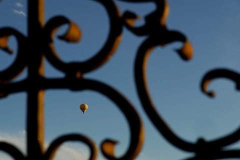 Yellow hot air balloon flying against a blue sky, seen through an ornate metal gate in ronda,