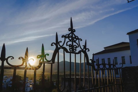 Sun shining through the ornate wrought iron gate at sunrise in ronda, spain, with mountains and