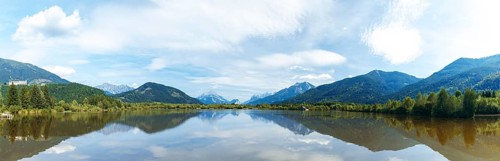 Panoramic lake reflects the surrounding mountains and the slightly cloudy sky, Admont, Styria,