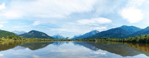 Panoramic lake reflects the surrounding mountains and the slightly cloudy sky, Admont, Styria,