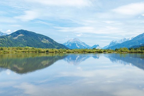 Panoramic lake reflects the surrounding mountains and the slightly cloudy sky, Admont, Styria,