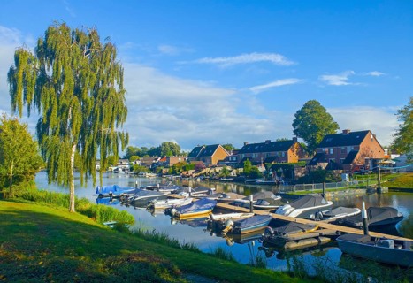 Small harbour with numerous boats on a sunny day, surrounded by trees and village houses,