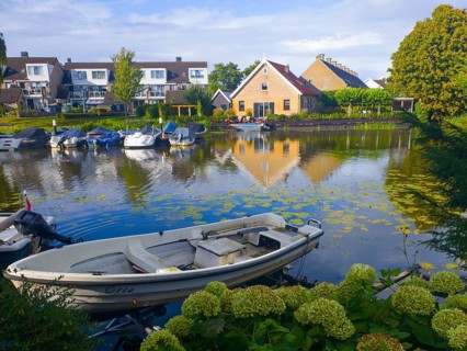 Boats on a quiet canal with reflection of houses in the water, surrounded by green landscape,
