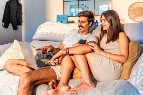 Young couple relaxing on comfortable sofa, browsing internet on laptop, enjoying time together in