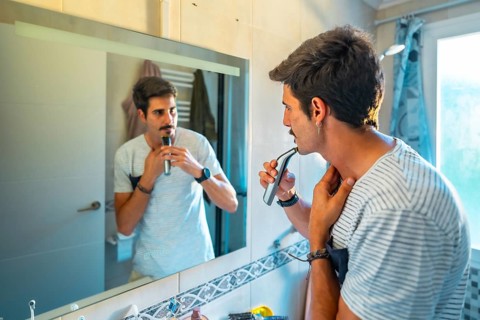 Caucasian man trimming his mustache with an electric razor while looking in the bathroom mirror