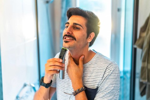 Man trimming his beard using an electric razor, taking care of his appearance in the bathroom