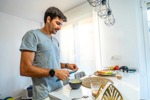 Young man spreading butter on fresh bread while enjoying breakfast in a bright, modern kitchen
