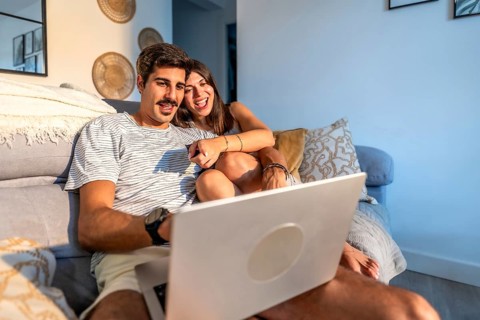 Young couple enjoying a movie on their laptop, laughing and having a good time together on the sofa
