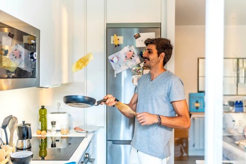 Young man flipping a pancake in a modern kitchen, enjoying a leisurely morning preparing breakfast