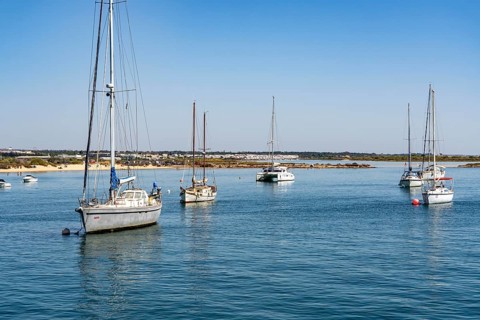 Sailboats anchored in the Gilão River, in front of the beach Praia da Ilha de Tavira, on the island