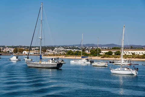 Sailboats anchored in the Gilão River, in front of the beach Praia da Ilha de Tavira, on the island