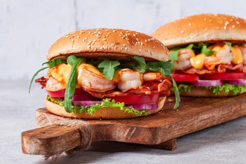 Two shrimp burgers and buns with sesame seeds, bacon, lettuce, tomatoes and onions, On a wooden