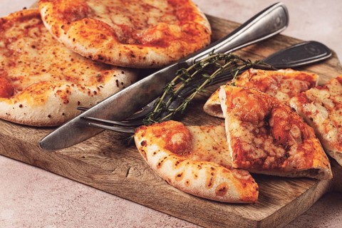 Four pizzetta Margaritas, on a cutting board, on a light gray surface, top view