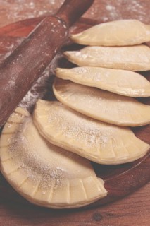 Raw chebureks, mini, on a cutting board, wooden table, close-up, no people