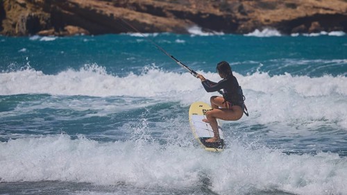 Kitesurfer spraying over waves in the blue sea, rocky coast in the background, Prasonisi, beach,