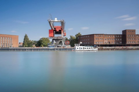 View over the Mittelland Canal to an industrial building and a crane in front of a ship, long