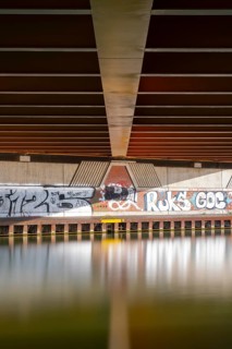 View across the Mittelland Canal to the underside and the graffiti-painted abutment of a bridge on