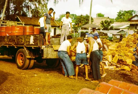 Male workers loading metal fuel drums onto back of lorry in timber yard, Johor Bahru, Johor,