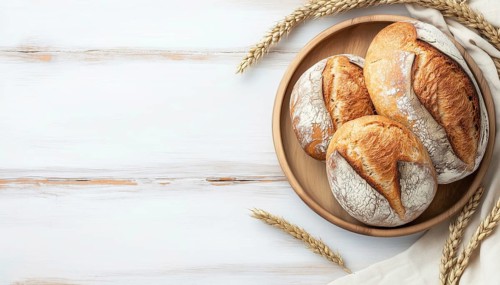 Top-View Presentation Of Fresh Bread On A Plate On A Light Wooden Surface With Copy Space For