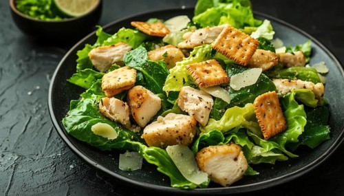Classic Caesar Salad With Crackers, Romaine Lettuce, And Grilled Chicken On A Black Plate: Side