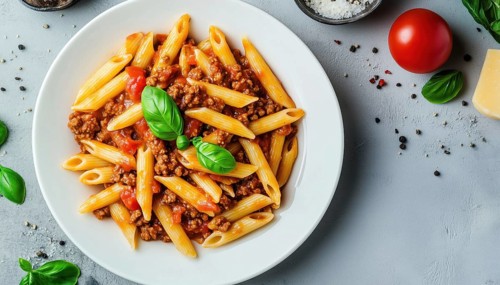 Delicious Penne Pasta With Bolognese Sauce And Fresh Basil On A White Plate Over A Light Background