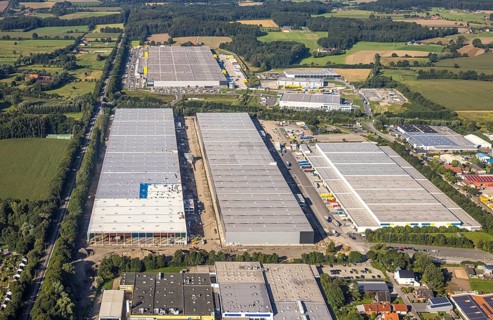 Large warehouses in an industrial area, framed by fields and scattered trees, aerial view Werl