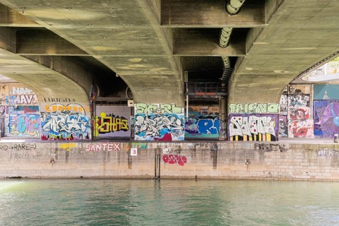 Under a bridge with various colourful graffiti over a river, Am Donaukanal Innere Stadt Vienna