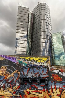 A modern high-rise building with a reflective glass façade and colourful graffiti in the foreground
