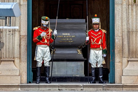 Two uniformed soldiers in red jackets stand guard in front of a marble building, Two soldiers guard