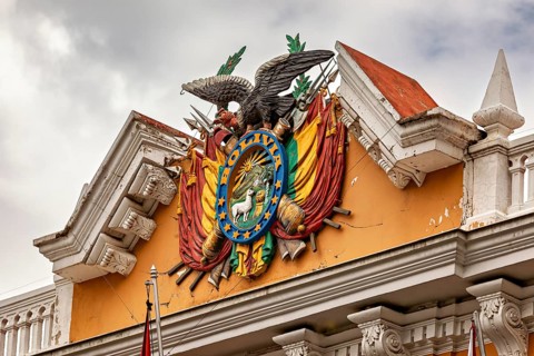 Detailed coat of arms with eagle on a historic building under a cloudy sky, The Presidential Palace