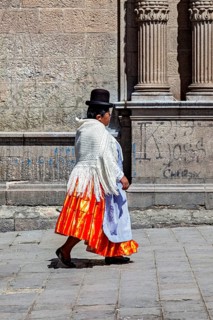 Woman in traditional dress with orange skirt walking along a historical wall, Traditionally dressed
