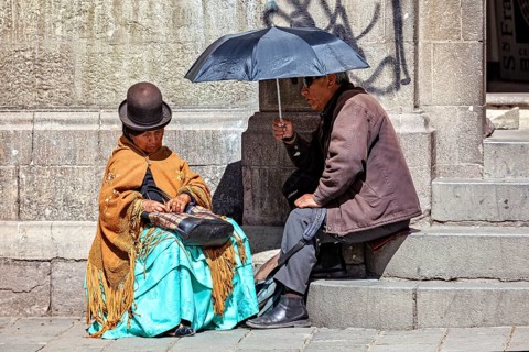 An elderly woman in traditional dress sitting and chatting with a man under an sunshade, A woman