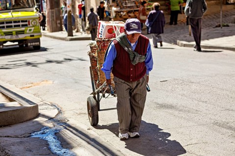 An elderly man pulls a handcart through a sunny city street, A man pulls a handcart through the