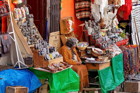 A woman in traditional dress sits at a market stall selling Andean souvenirs, the witches' market