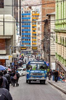 Busy city street with a blue bus and many people during the day in the middle of tall buildings, A