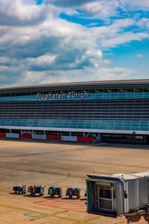 Zurich Airport and Building and Boarding Bridge Gate and Lugage on Trailer on Airfield in a Sunny