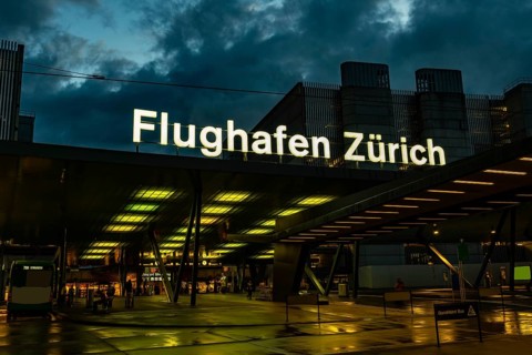 Illuminated Entrance Sign to Zurich Airport and a Bus Station at Night in the Airport in Kloten,