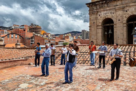 Group of musicians on a tiled roof in front of an urban backdrop with clouds in the sky, A music