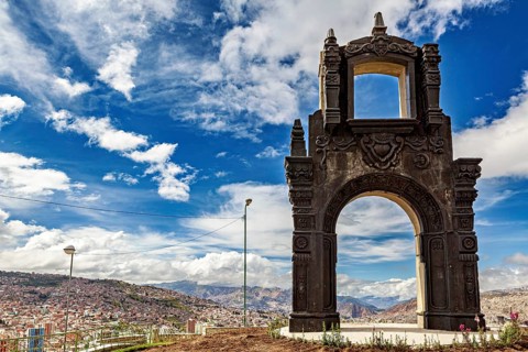 An artistically designed stone gate with a view of a city and clouds in the sky, The gate at the