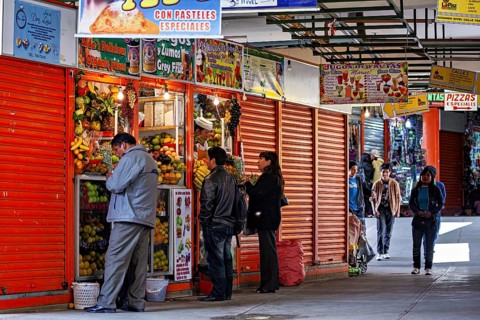 Busy market with people buying fresh vegetables and other food, small shops and restaurants in the