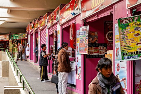 Row of pink market stalls with colourful signs, people ordering food, small shops and restaurants