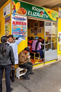 Small food stall with yellow walls, people sitting and eating, menu posters on the wall, Small