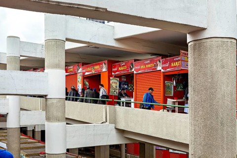 People walk through the upper floors of a modern market with red facades, Small shops and