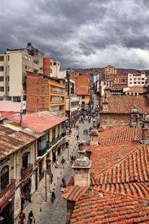 Historic city view with red tiled roofs under a cloudy sky, people in the streets of La Paz in
