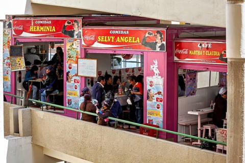 Lively food stalls with smiling people and Coca-Cola adverts, convivial atmosphere, small shops and