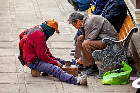 A shoeshine boy works on a pavement polishing the shoes of a seated man, shoeshine boy in the