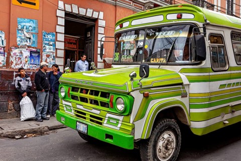 Green retro bus in front of a municipal building with people on the pavement, The colourful buses