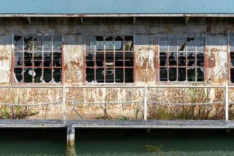 Abandoned building with broken windows and rust next to a body of water, at the harbour of Linz