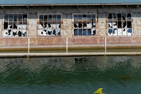 Dilapidated building with broken windows and rusty structures on the waterfront, at Linz harbour